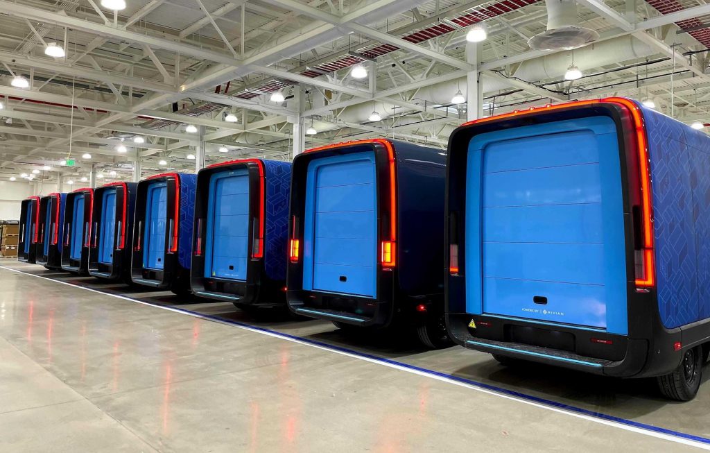 Rows of commercial electric delivery vans staged inside an enterprise fleet depot