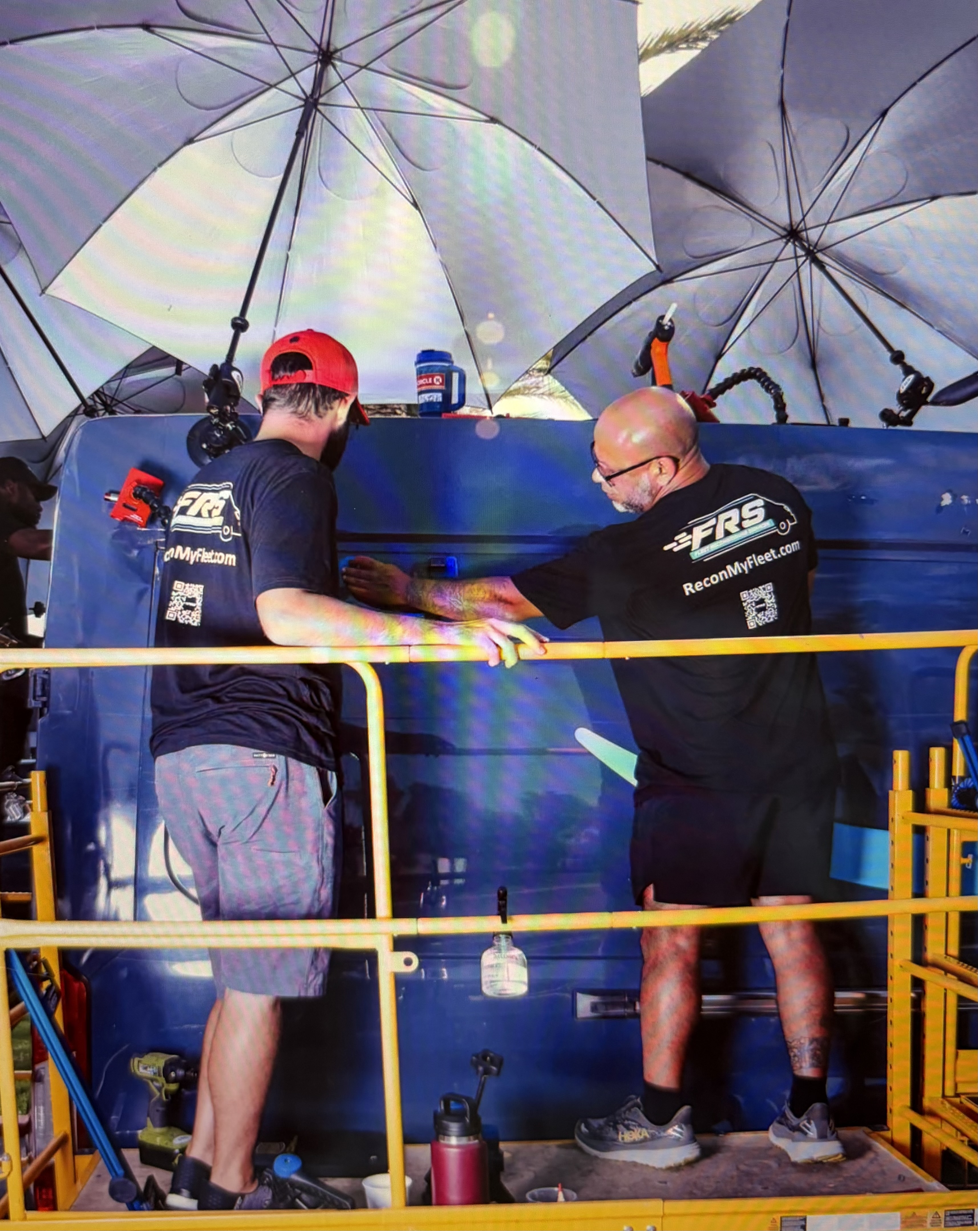 Two FRS technicians on a scissor lift reconditioning the roof of an Amazon delivery van under work umbrellas