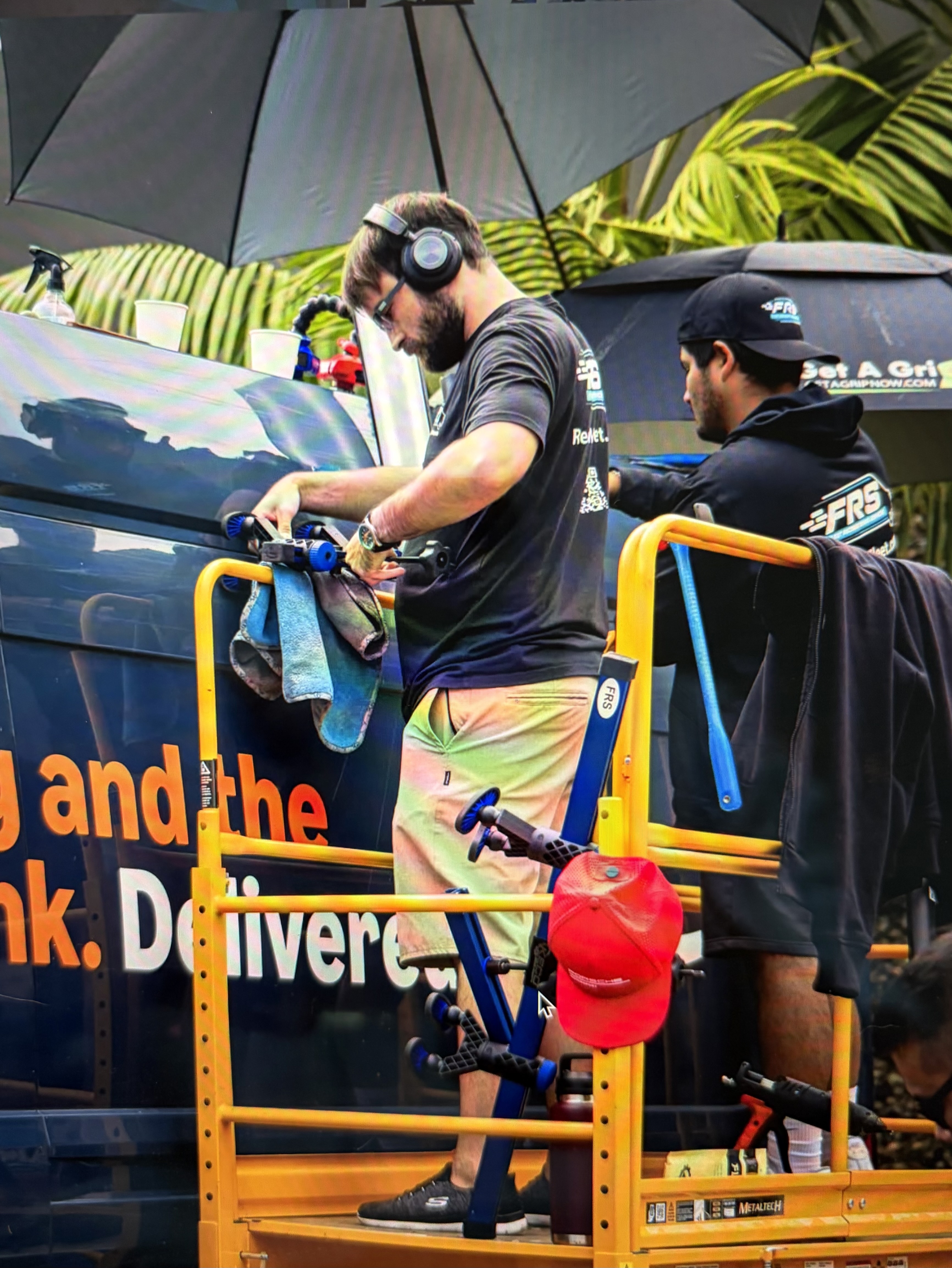 FRS technicians working on the upper panels of a wrapped commercial van from a raised platform