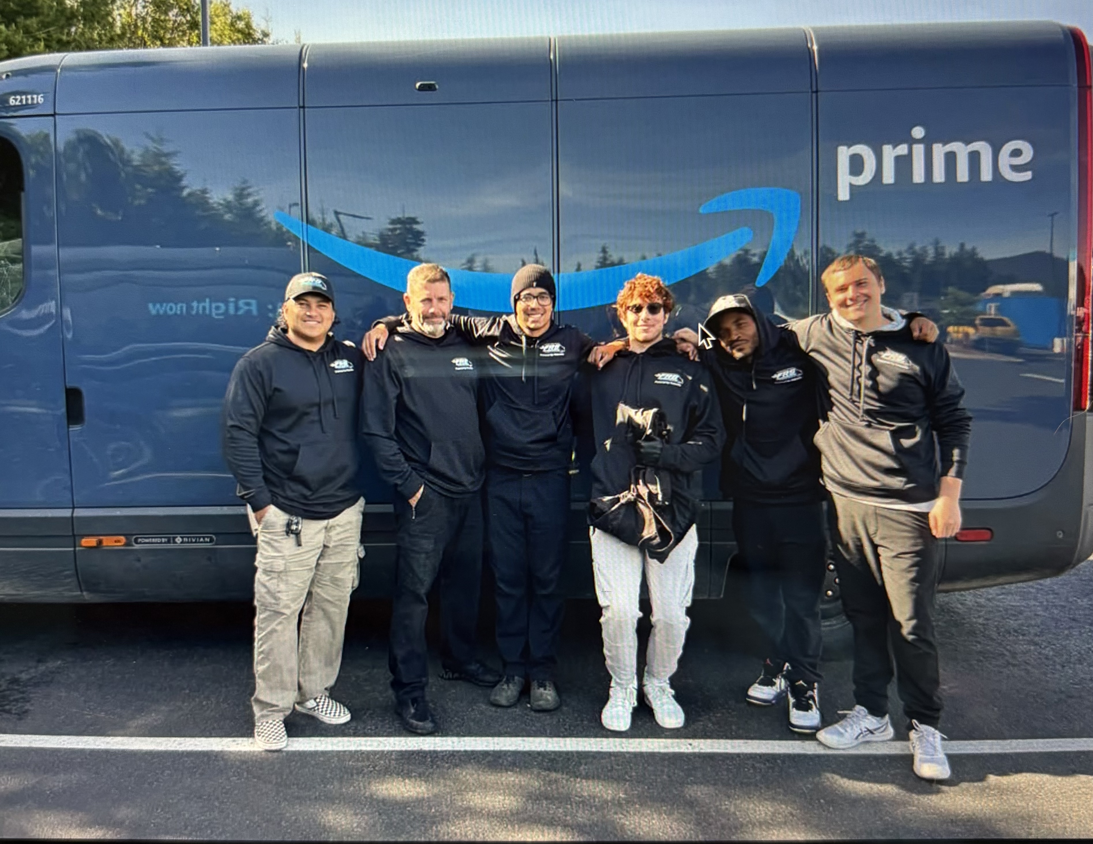 Six FRS team members standing together in front of an Amazon Prime electric delivery van