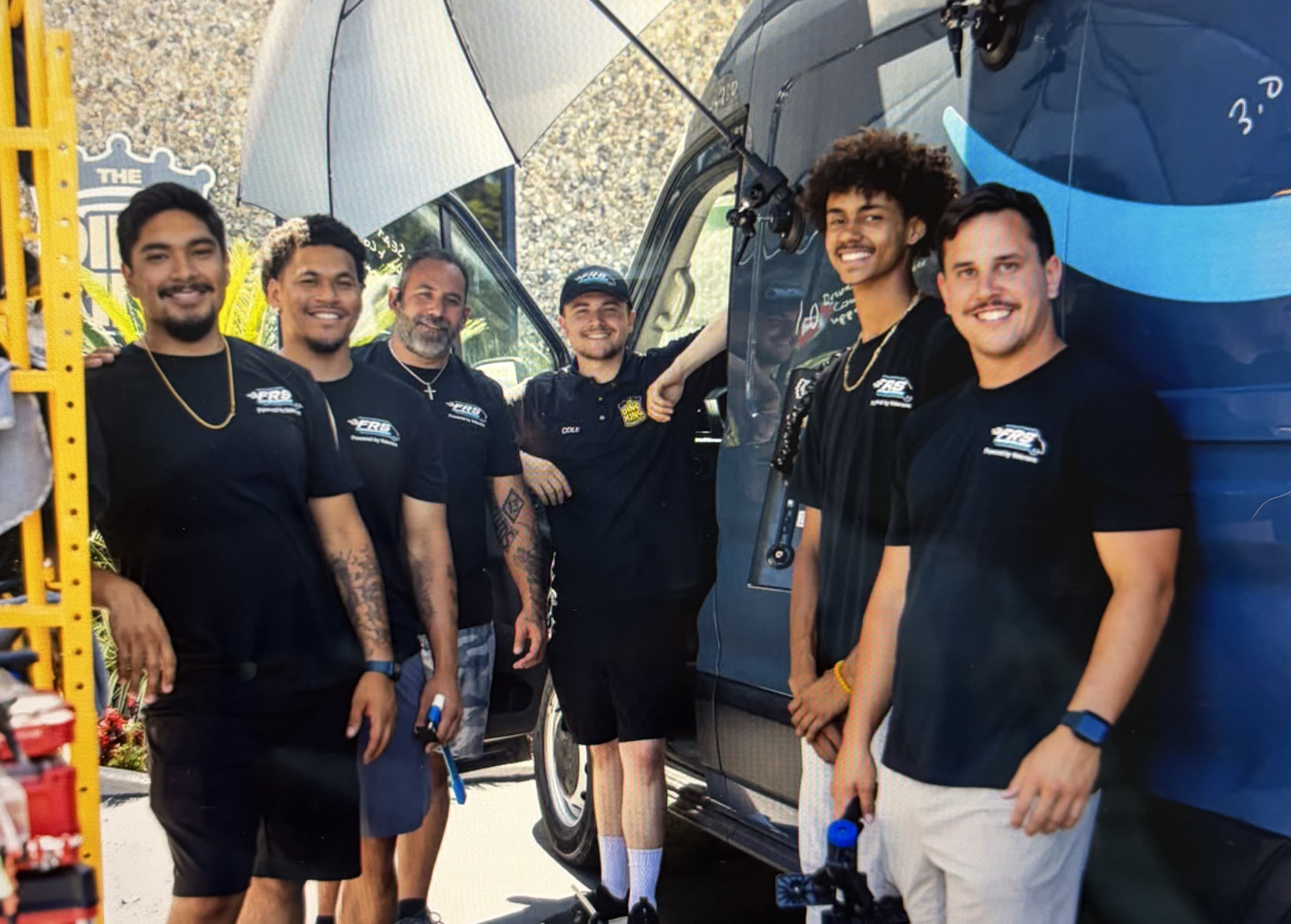 FRS crew gathered and smiling in front of a dark Amazon delivery van at a work site