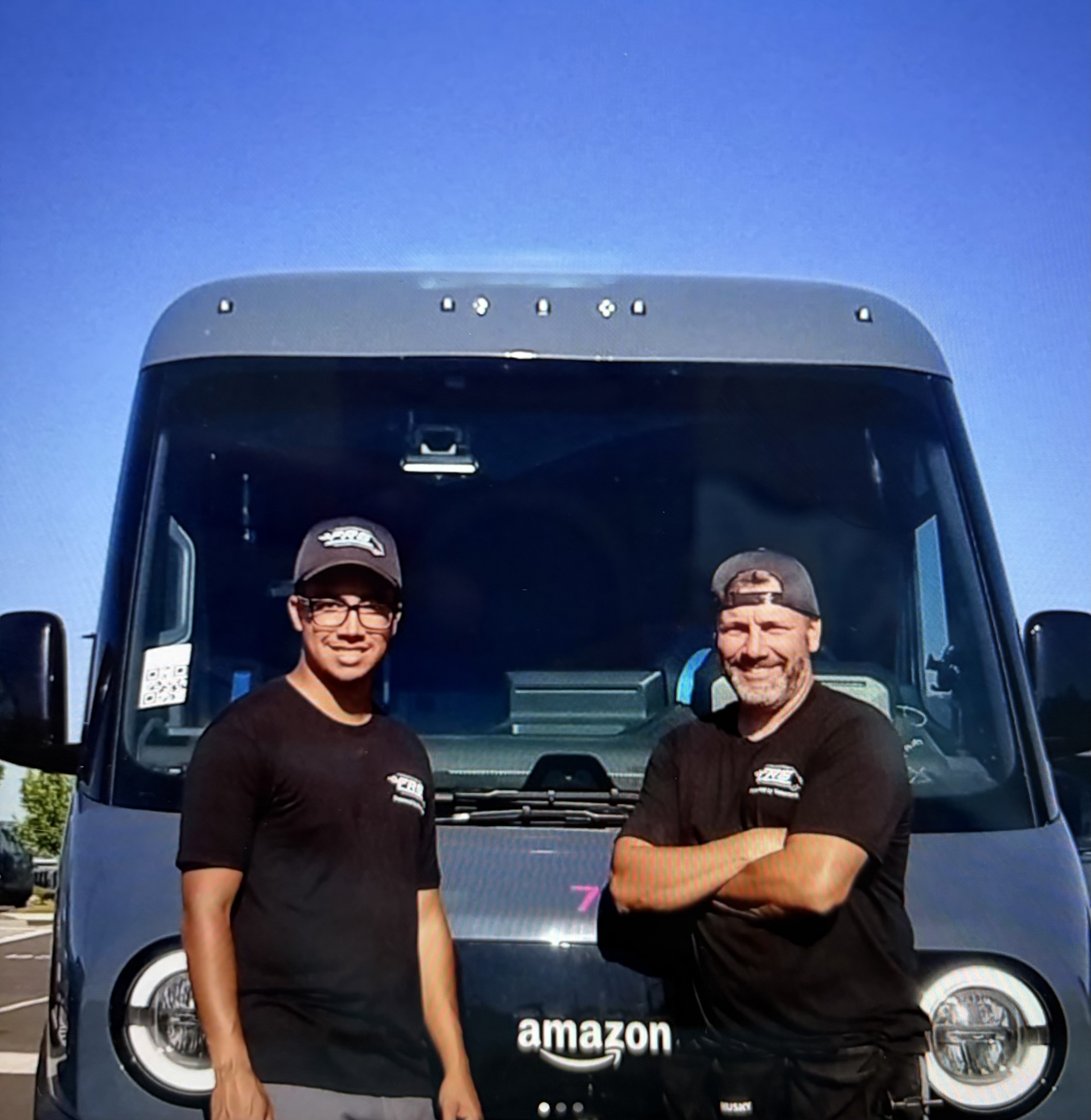 Two FRS team members smiling at the front of an Amazon delivery van