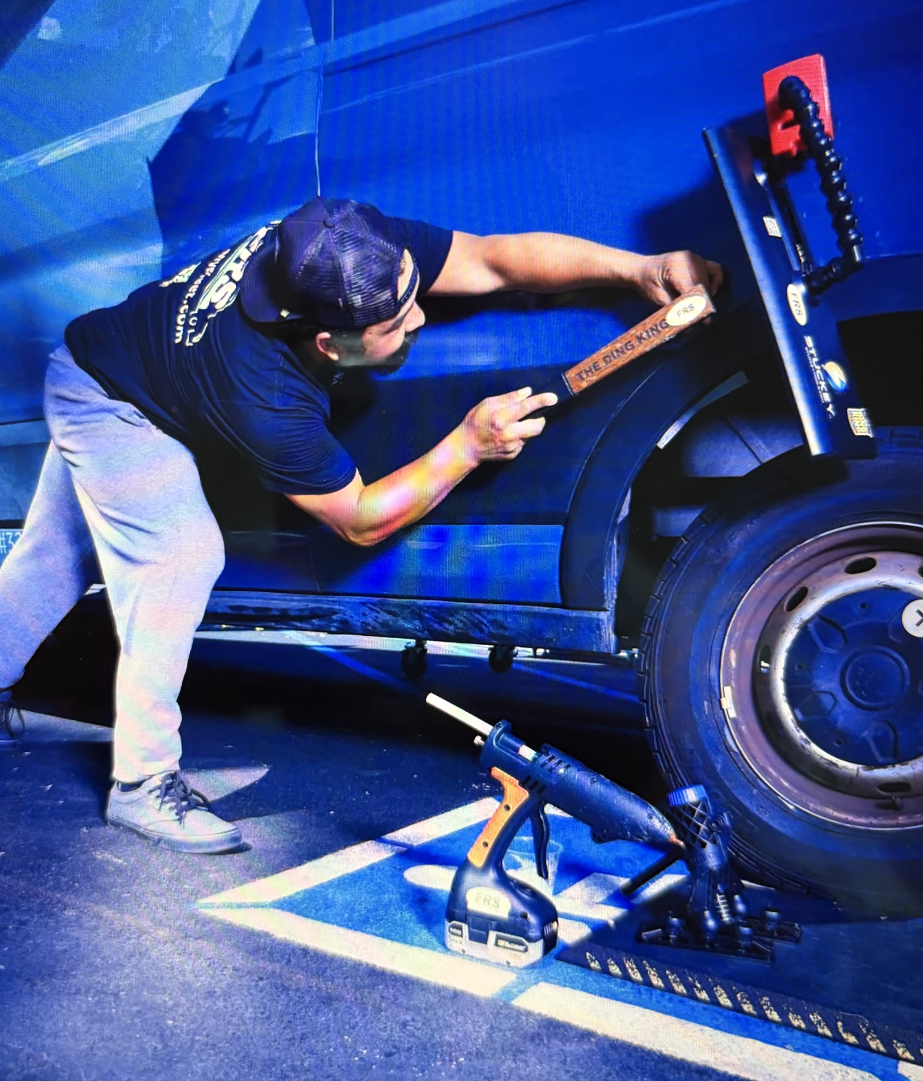 An FRS technician performing paintless dent repair on a van panel under dramatic blue lighting