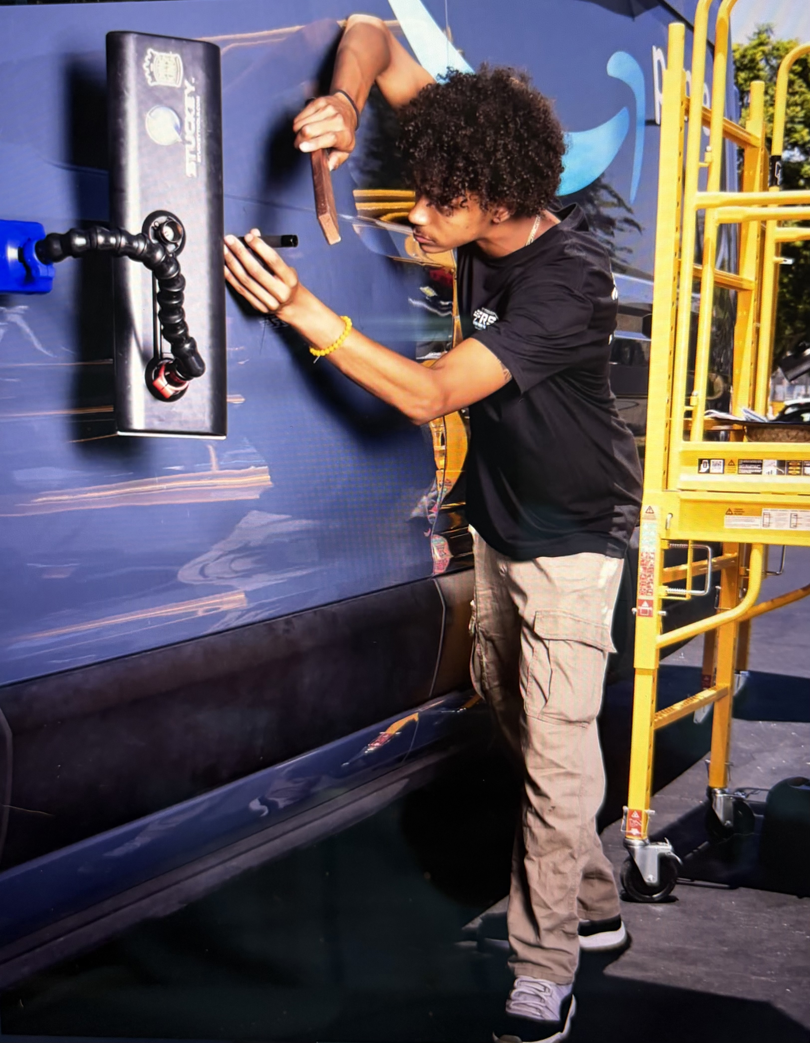 An FRS technician repairing the side panel of an Amazon Prime van beside a mobile work lift