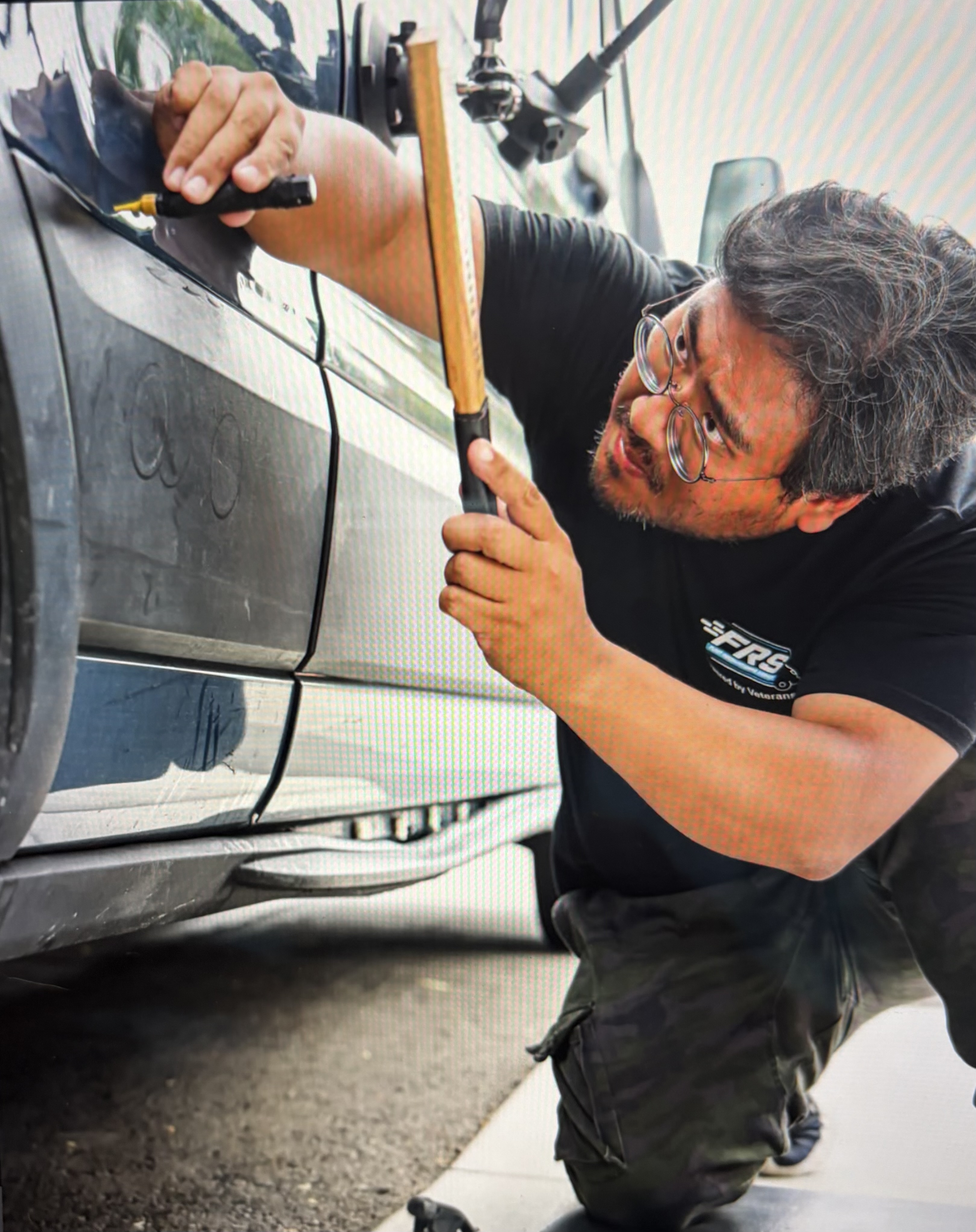 An FRS technician in Powered by Veterans apparel performing paintless dent repair on a fleet van